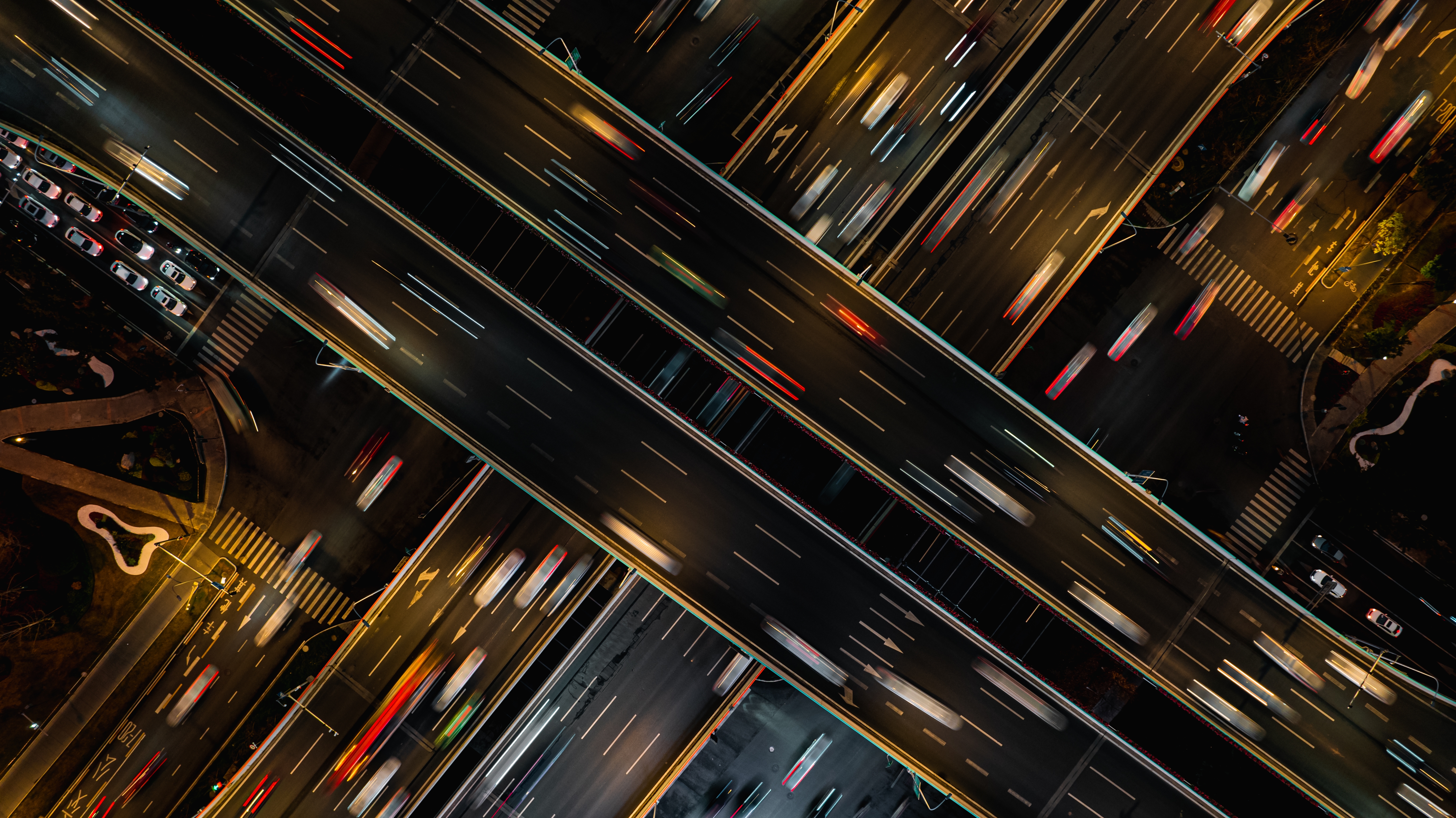 Aerial view of a busy city highway at night with streaks of light from moving vehicles, illustrating fast-paced urban transportation and traffic flow.